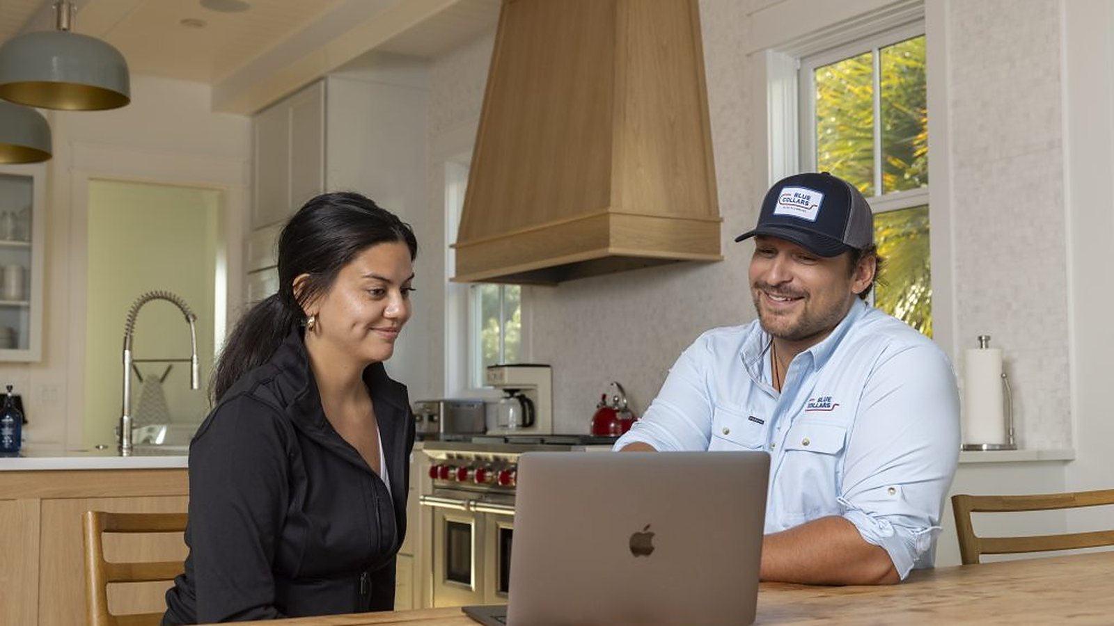Blue Collars technician and a homeowner sitting together at a kitchen table looking at a laptop in a bright Charleston kitchen